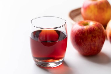 Beyaz arka planda kırmızı elma meyveli bir bardak elma şarabı.