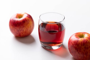 Beyaz arka planda kırmızı elma meyveli bir bardak elma şarabı.