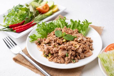 Yerel Tayland yemekleri, baharatlı domuz salatası (Larb Moo) beyaz arka planda taze sebzelerle yemek