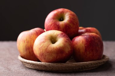 Siyah arkaplanlı kahverengi kumaş üzerinde kırmızı elma (Envy apple) sepeti