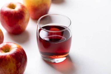 Beyaz arka planda kırmızı elma meyveli bir bardak elma şarabı.