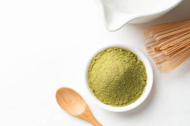 Tahta kaşıklı kibrit yeşil çay tozu, bambu çırpısı ve beyaz arka planda Chawan kasesi.
