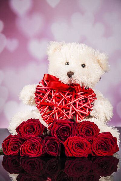 Teddy bear mascot and red roses and red wicker heart for valentine's day.