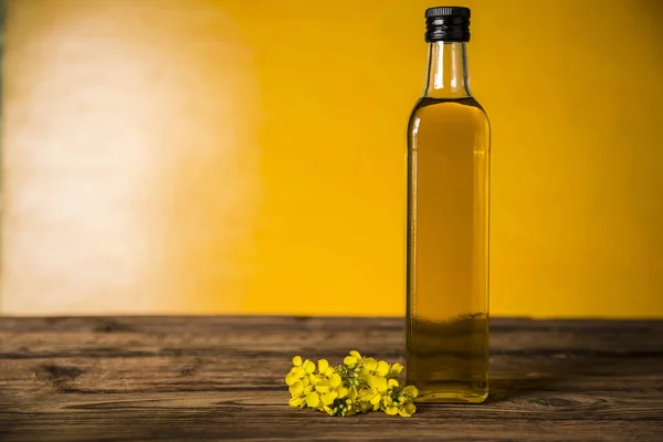 Flores de colza y aceite de colza en una botella sobre la mesa — Foto de Stock