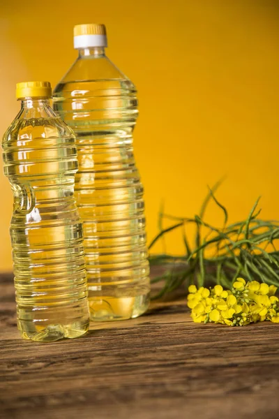 Flores de colza y aceite de colza en una botella sobre la mesa — Foto de Stock