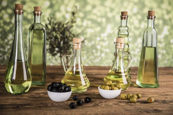 Olijfolie, olijfboom en groene en zwarte olijven op een houten tabblad — Stockfoto