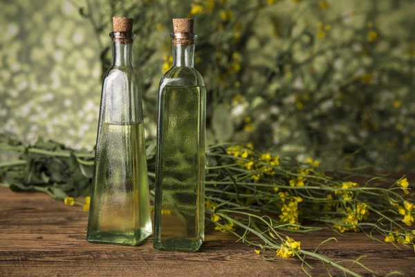 Flores de colza y aceite de colza en una botella sobre la mesa — Foto de Stock