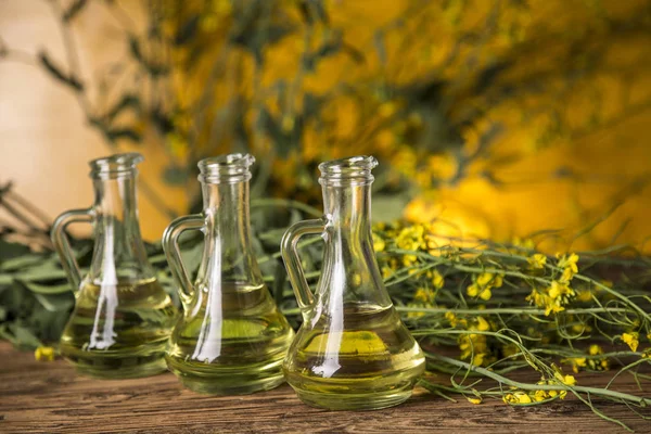 Flores de colza y aceite de colza en una botella sobre la mesa — Foto de Stock