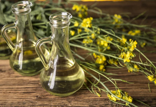 Flores de colza y aceite de colza en una botella sobre la mesa — Foto de Stock