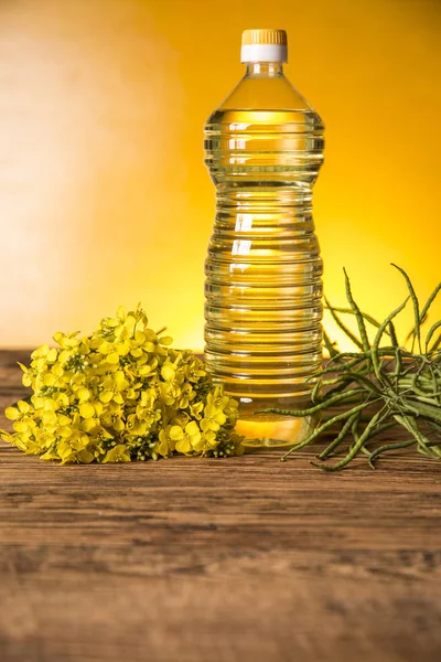 Flores de colza y aceite de colza en una botella sobre la mesa —  Fotos de Stock