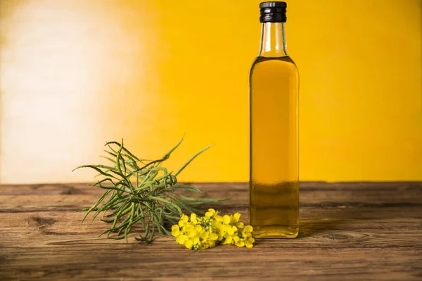 Rapeseed flowers and rapeseed oil in a bottle on the table — Stock Photo, Image