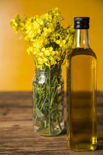 Flores de colza y aceite de colza en una botella sobre la mesa — Foto de Stock