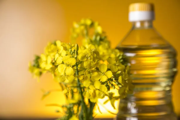 Flores de colza y aceite de colza en una botella sobre la mesa — Foto de Stock