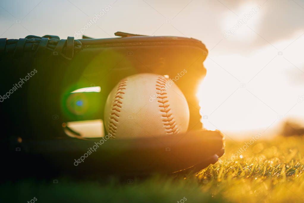 Baseball in glove in the lawn at sunset in the evening day with sun ray and lens flare light