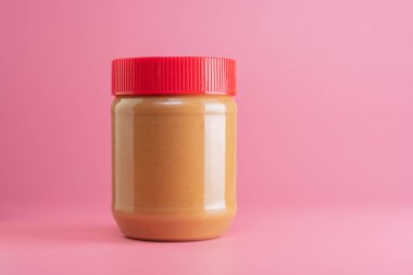 Fıstık ezmesi kavanozunu kapatın. Pembe arka planda izole edilmiş.