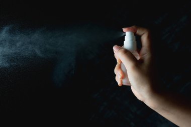 Elinde küçük bir sprey şişesi olan ve arka planına sprey sıkan bir kadın.