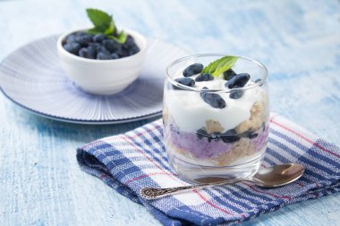 Peynirli krem peynirli cheesecake keki ve mavi bir arka planda mavi bir peçetede cam bir bardakta hanımeli çilek.