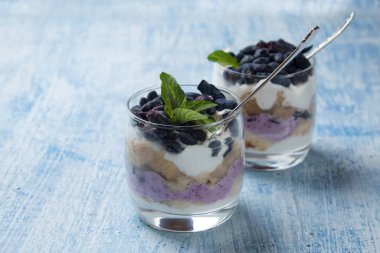 İki bardak krem peynirli ve hanımeli meyveli kek açık mavi arka planda duruyor.