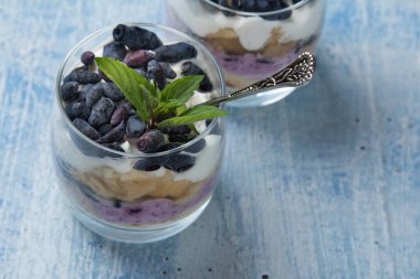 Peynir kremalı cheesecake keki, hanımeli böğürtlen, mavi arka planda bardakta nane yaprağı.