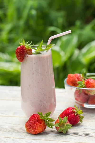 新鲜草莓的奶昔矗立在轻盈的木制背景上 草莓在桌子上和透明的花瓶里 — 图库照片