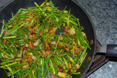 Koyu bir tavada soğanlı ve havuçlu kızarmış fasulye.