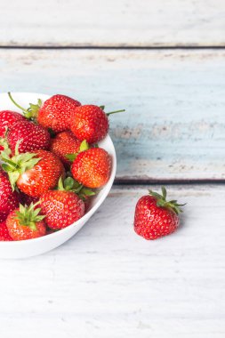 Olgun çilekler açık ahşap bir zemin üzerinde duran beyaz yüksek bir tabakta yatar. Kopyalama alanı