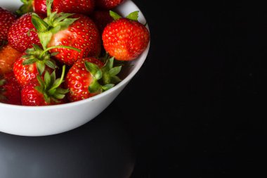 Birkaç olgun çilek siyah camlar üzerinde beyaz bir tabakta uzanıyor. Uzay kopyası için bir yer.