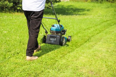 Bir adam kendi kır evindeki çimleri biçer.