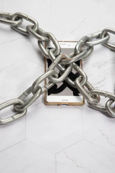 Beyaz arka planda büyük metal zincirli beyaz akıllı telefon. Dijital detoksifikasyon, teknolojiye bağımlılık, cihaz ve cihaz eksikliği. Kopya alanının yeri.