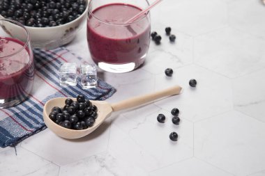 Hafif bir arka planda böğürtlenli ahşap bir kaşık, mavi bir peçetede iki bardak yaban mersinli meyve suyu var. Kopyalama alanı