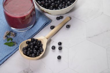 Hafif bir arka planda böğürtlenli ahşap bir kaşık, mavi bir peçetede iki bardak yaban mersinli meyve suyu var. Kopyalama alanı