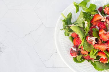Beyaz tabakta çilekli yaz salatası ve hafif bir arka plan. Kapatın. Kopyalama alanı