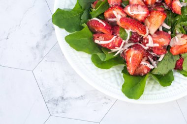 Beyaz bir tabakta çilekli ve yeşillikli yaz salatası ve hafif bir arka plan. Kapatın. Kopi alanı için bir yer. Dikey yönelim