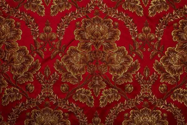Kumaş deseninde tekrar eden çiçek deseni ve geometrik elementler var. Kırmızı kumaş rengi. Metalik ipliklerle işlenmiş nakış