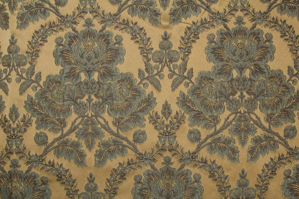 Kumaş deseninde tekrar eden çiçek deseni ve geometrik elementler var. Bej kumaş rengi. Metalik ipliklerle işlenmiş nakış
