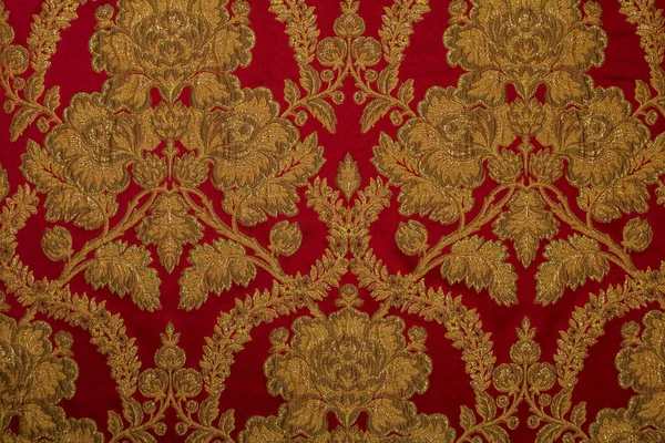 Kumaş deseninde tekrar eden çiçek deseni ve geometrik elementler var. Kırmızı kumaş rengi. Metalik ipliklerle işlenmiş nakış