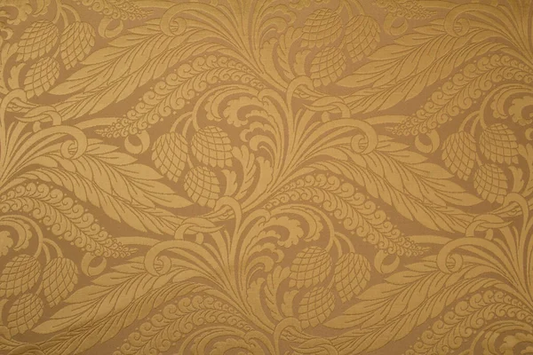 Kumaş deseninde tekrar eden çiçek deseni ve geometrik elementler var. Bej kumaş rengi. Metalik ipliklerle işlenmiş.