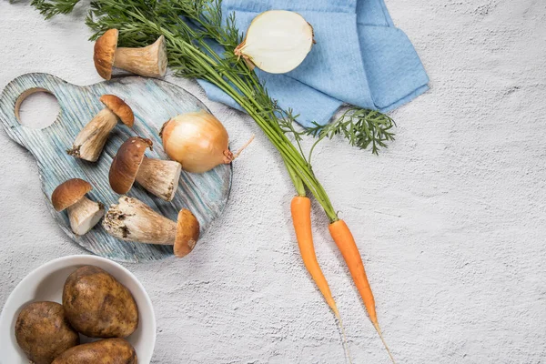 Ingredients for cooking mushroom soup-porcini mushrooms, onions, carrots, potatoes on a light background. Russian cuisine. Vertical orientation. Place for copy space