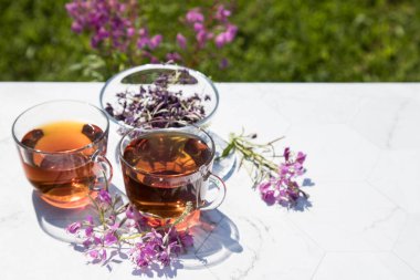 Chamaenerion angustifolium çayı (selvi, büyük söğüt, pembe söğüt) açık arkaplanda cam bardaklarda süslemek için kuru ve taze çiçekler ile birlikte. Bitkisel ilaç kavramı. Yatay yönelim