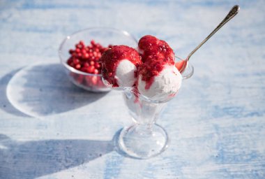 Dondurma toplarıyla dolu bir kase ve mavi arka planda kırmızı böğürtlenlerden reçel cam vazoda böğürtlenler, masada güneş gölgeleri. Yatay yönelim