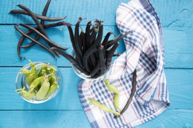Ahşap arka planda cam bardaklarda yeşil bezelye ve çalı fasulyesi kabukları. Bitki proteinlerinin kaynağı. Sağlıklı beslenme kavramı.