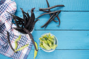 Mavi ahşap arka planda cam bardakta yeşil bezelye ve kuşkonmaz fasulyesi kabukları. Sebze proteinin kaynağı