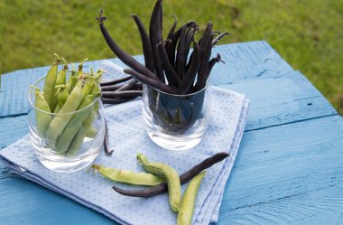 İki cam bardak, yeşil bezelye ve fasulyeli mavi peçete ve ahşap zemin. Sebze proteinin kaynağı