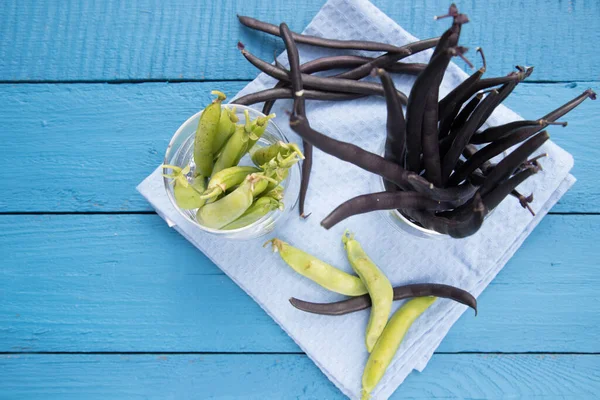 Mavi ahşap arka planda cam bardakta yeşil bezelye ve kuşkonmaz fasulyesi kabukları. Fotokopi için bir yer. Sebze proteinin kaynağı