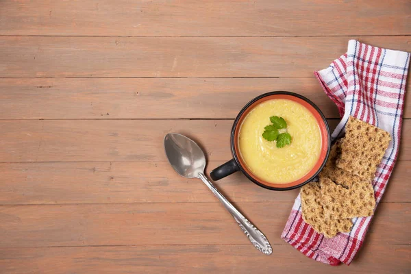 A plate of pumpkin soup, grain loaves on a red napkin and a brown wooden background . Horizontal orientation. Place for a copy space
