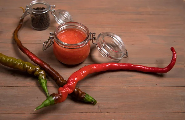 Hot sauce and black pepper peas in glass jars, hot pepper pods on a brown wooden background.Horizontal orientation