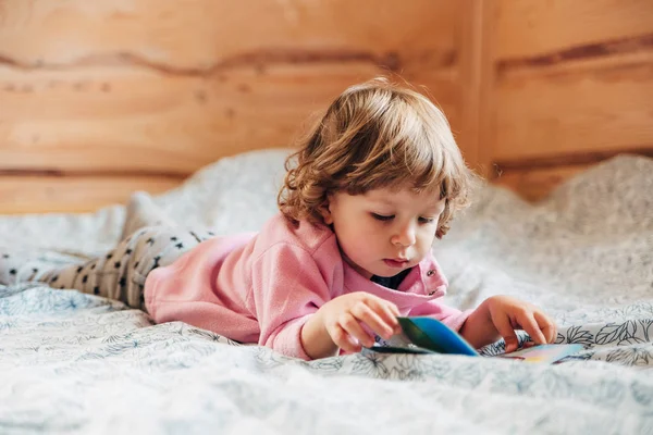 Aranyos kis lány az ágyban könyvével. — Stock Fotó