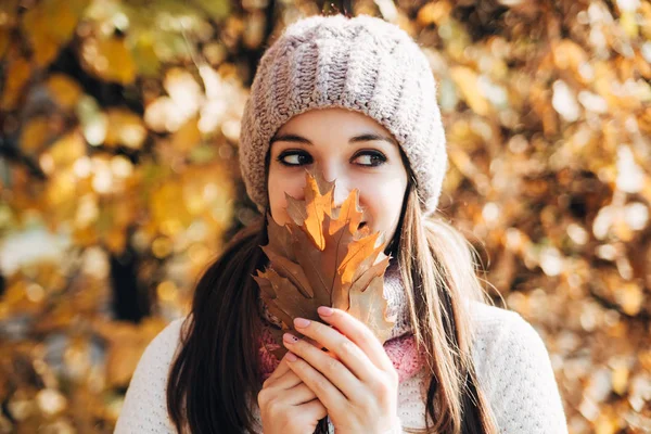 A boldog csinos barna lány portréja kötött pulóvert és kalapot visel az őszi parkban. Ragyogó napsütéses nap. Jó pozitív hangulat. Narancs és sárga elesett levelek háttér — Stock Fotó