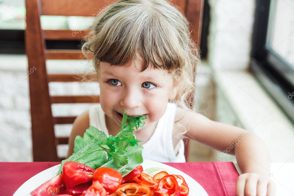 Funny child girl with big eyes eating vegetables salad