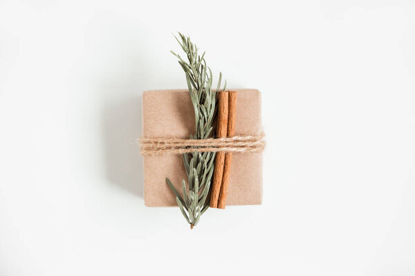Flat lay of Christmas craft gift box on the white background. Hand made brown paper box with Christmas tree branch and cinnamon sticks. Christmas composition.
